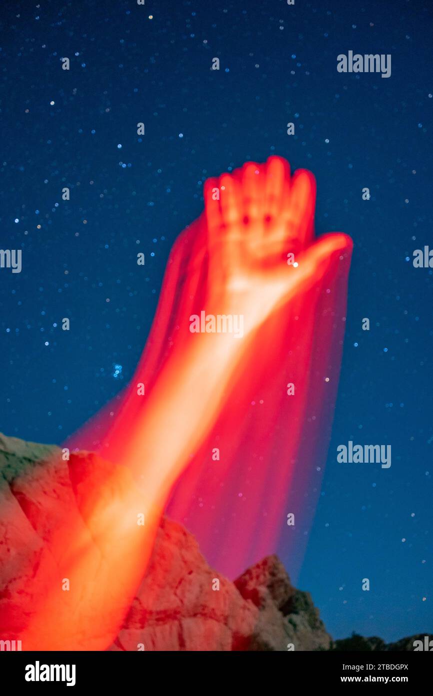Arms reaching and waving in red light taken with a starry desert landscape in the background. Stock Photo