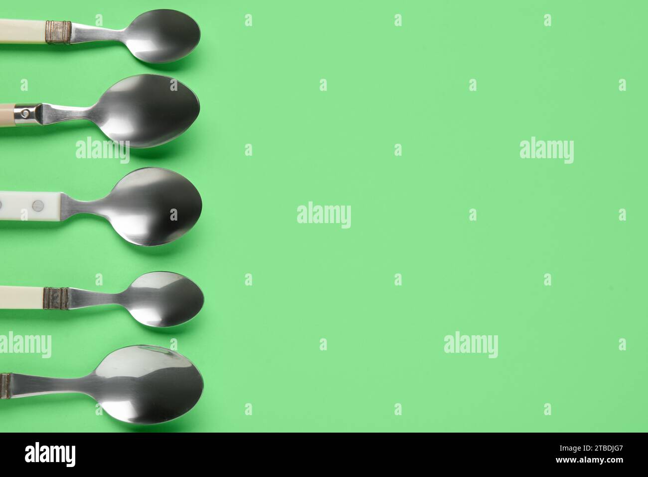 Different metal spoons on green background Stock Photo - Alamy