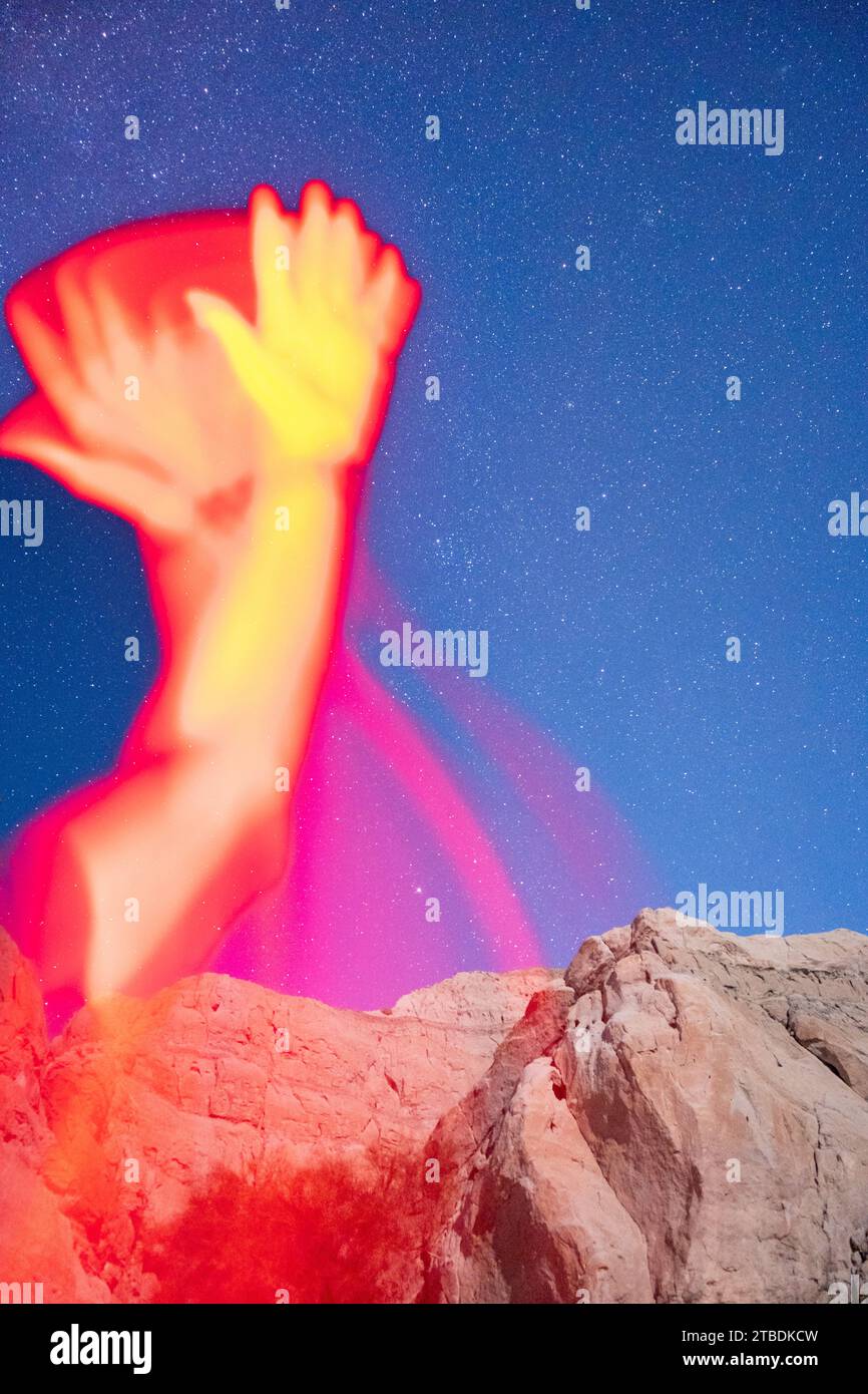 Arms reaching and waving in red light taken with a starry desert landscape in the background. Stock Photo