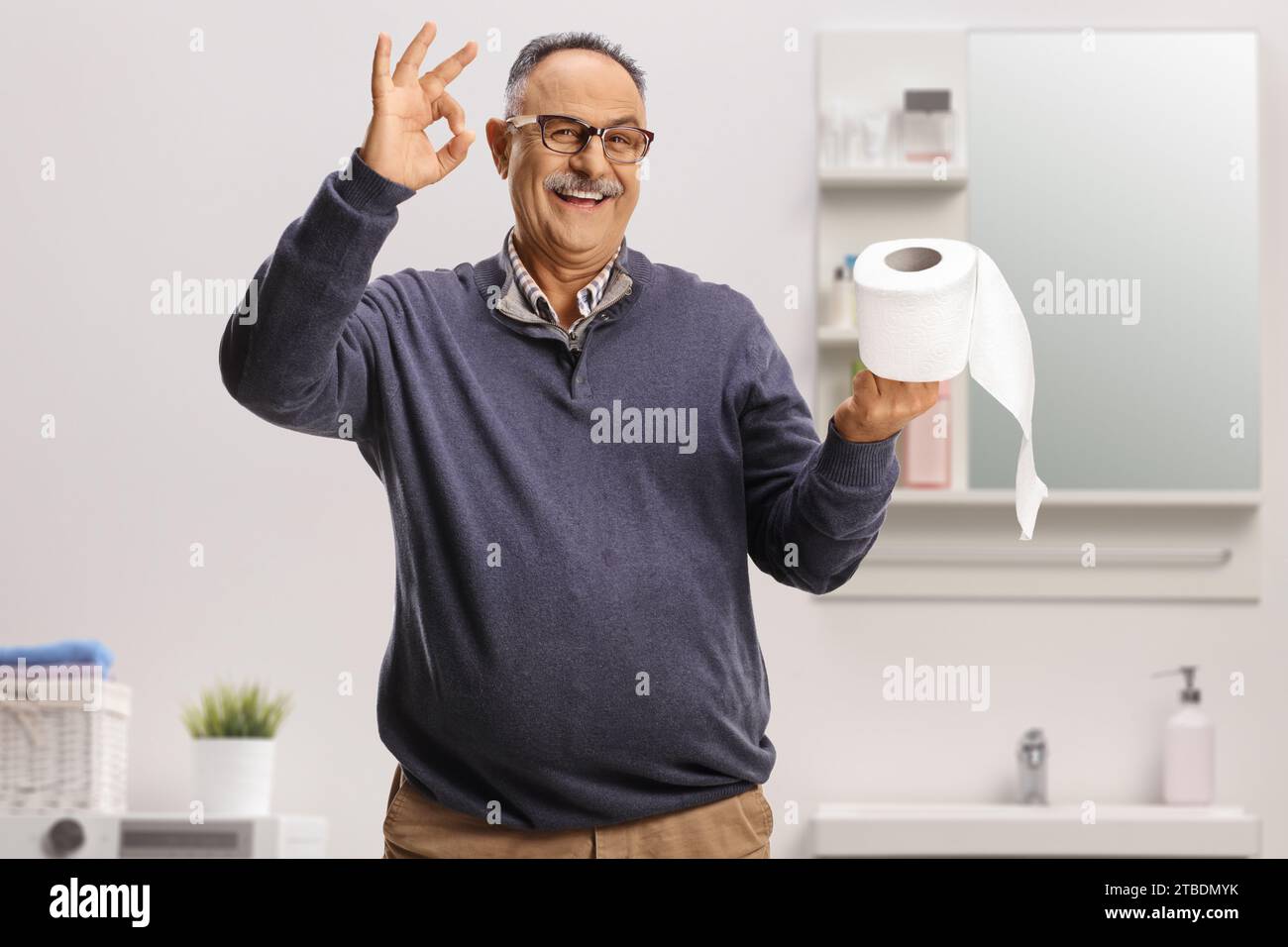 Smiling mature man holding a toilet paper roll and gesturing ok sign