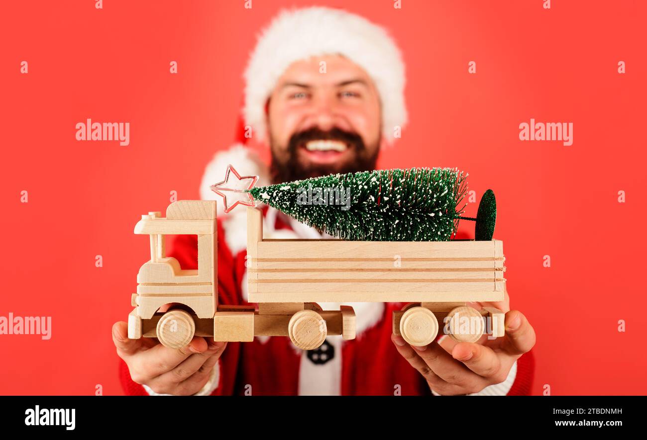Christmas tree with star on wooden toy truck car. Smiling Santa Claus holds toy car with Christmas tree. Christmas holiday celebration. Delivery of Stock Photo