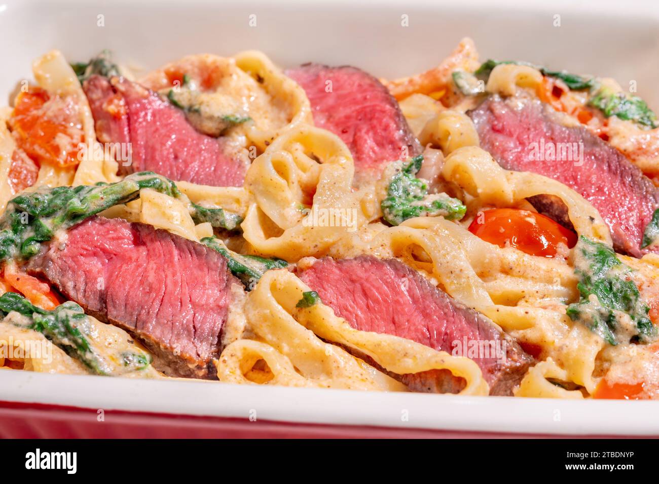Creamy steak fettuccine pasta with spinach and tomatoes Stock Photo