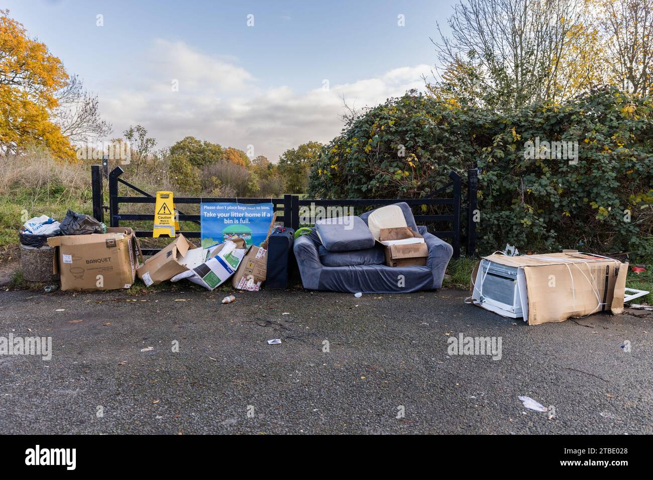 A fly tipping site including cardboard boxes, a couch, suitcase and fridge freezer by a 'Take Your Litter Home' banner. Photo by Amanda Rose/Alamy Stock Photo