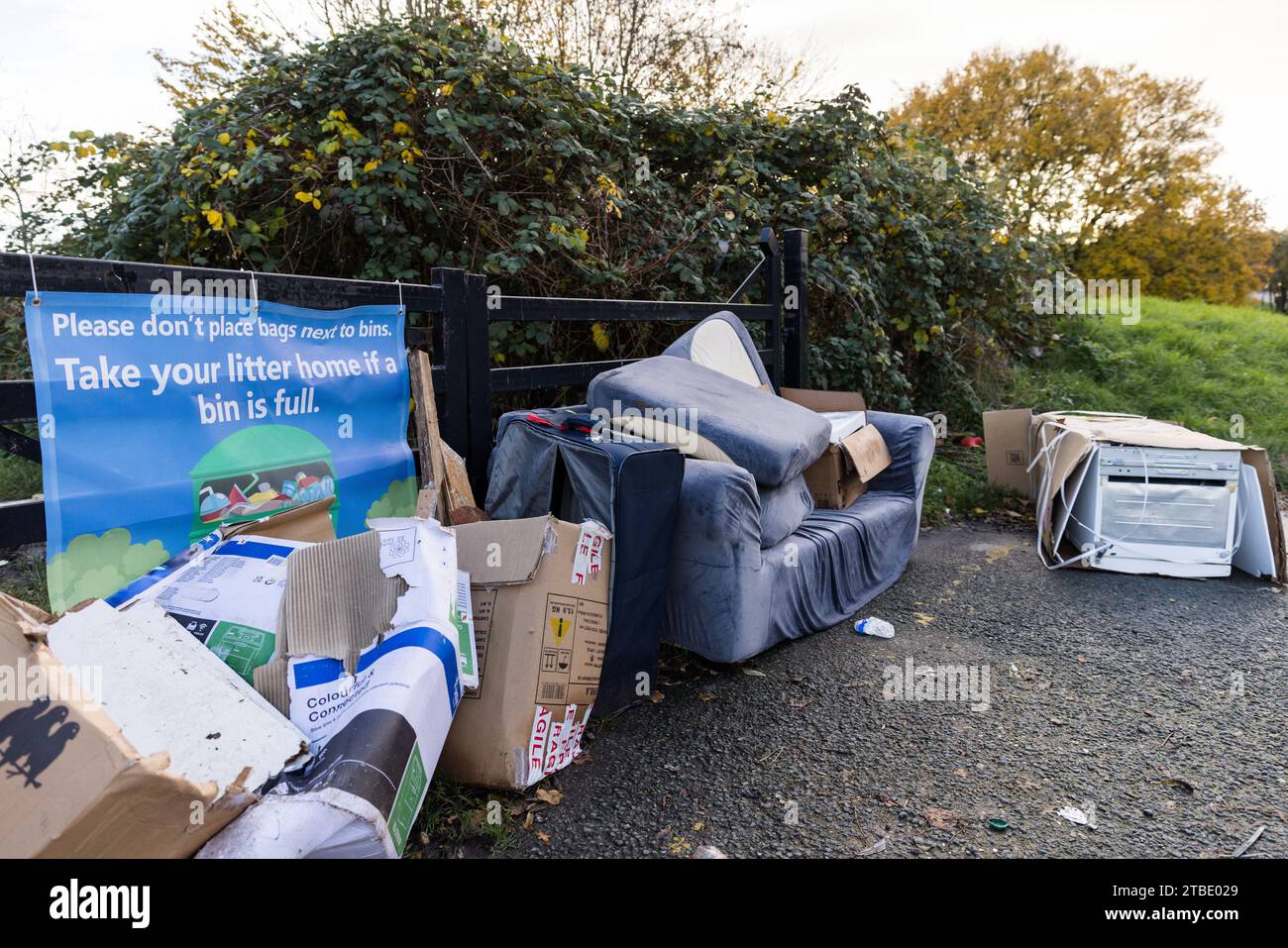 A fly tipping site including cardboard boxes, a couch, suitcase and fridge freezer by a 'Take Your Litter Home' banner. Photo by Amanda Rose/Alamy Stock Photo