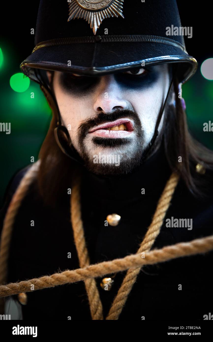 A close up portrait of a male cosplayer at a comic con event in a scary British Police uniform with white painted face in a Halloween concept Stock Photo