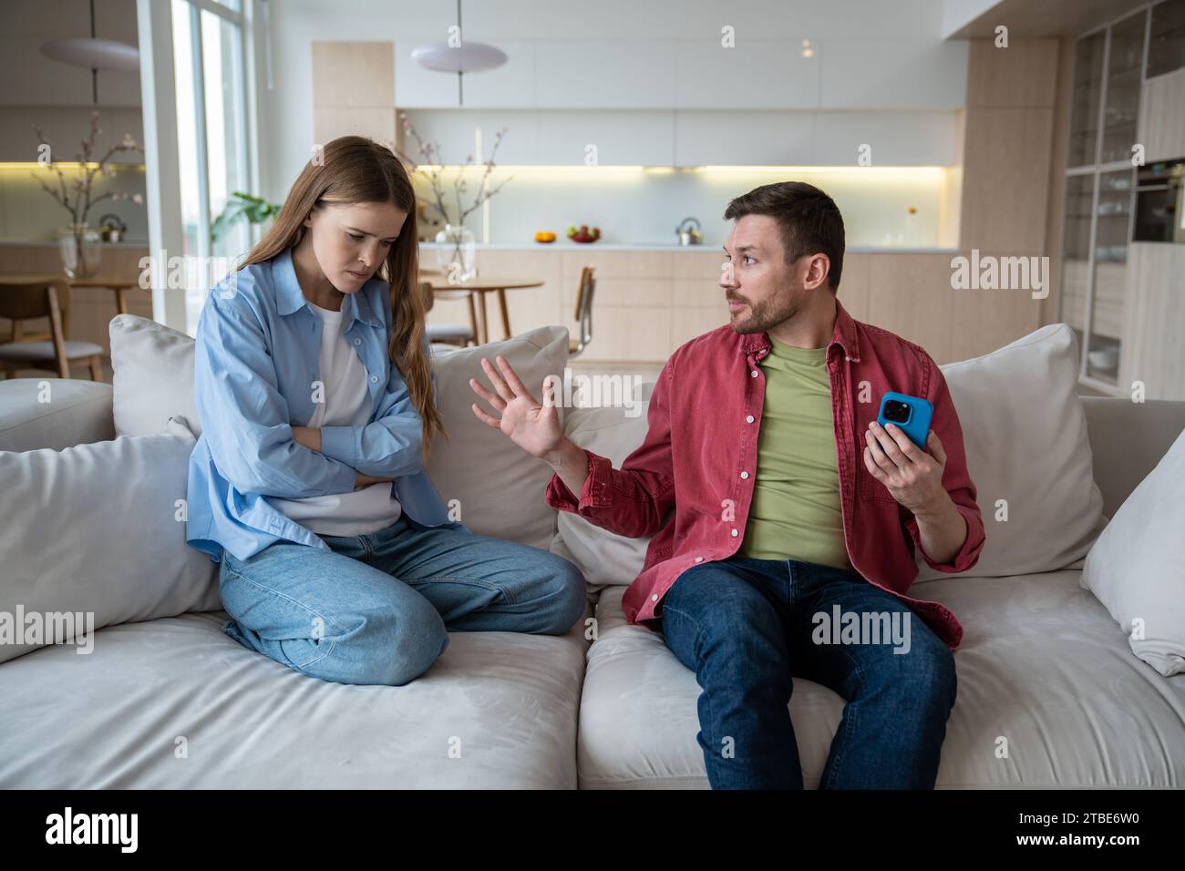 Offended wife suspecting husband of unfaithfulness, man hiding phone display, justifying situation  Stock Photo