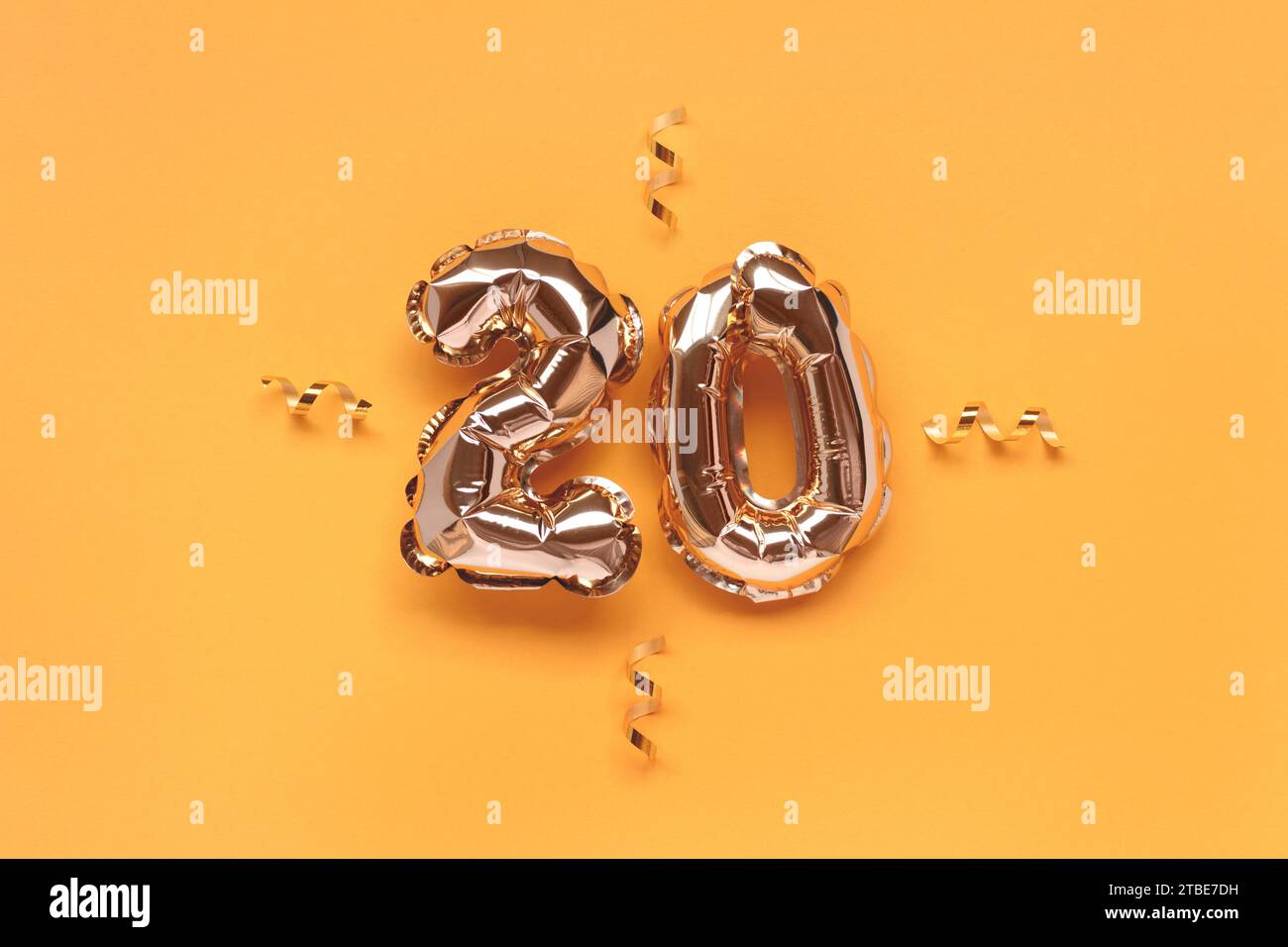 Number twenty gold foil balloons with ribbon confetti on a golden background. Stock Photo