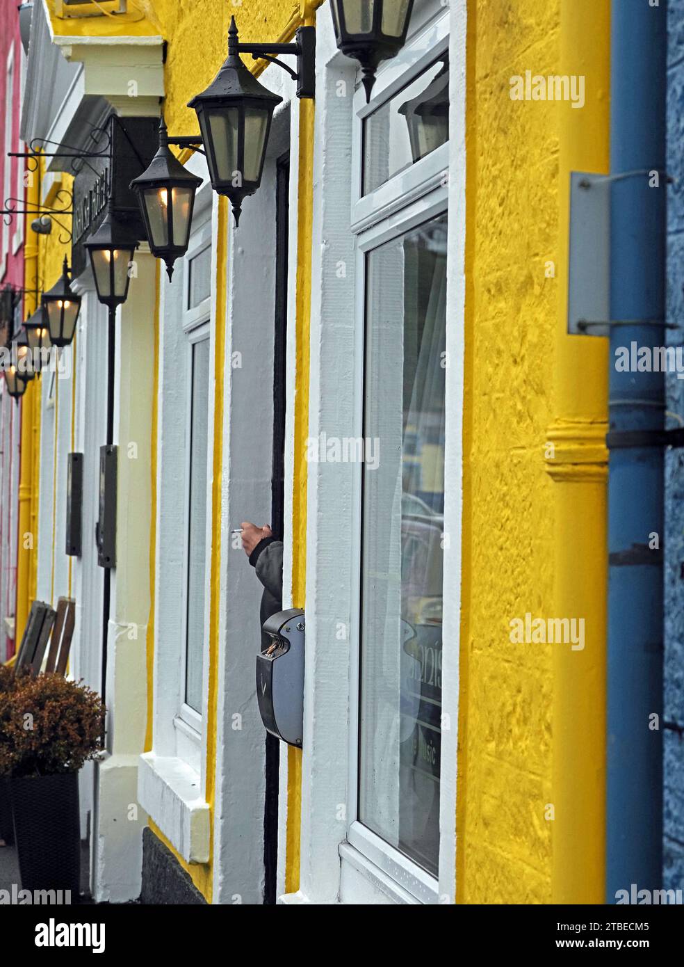 anonymous smoker's hand with cigarette among brightly painted facades of blue, yellow & red with