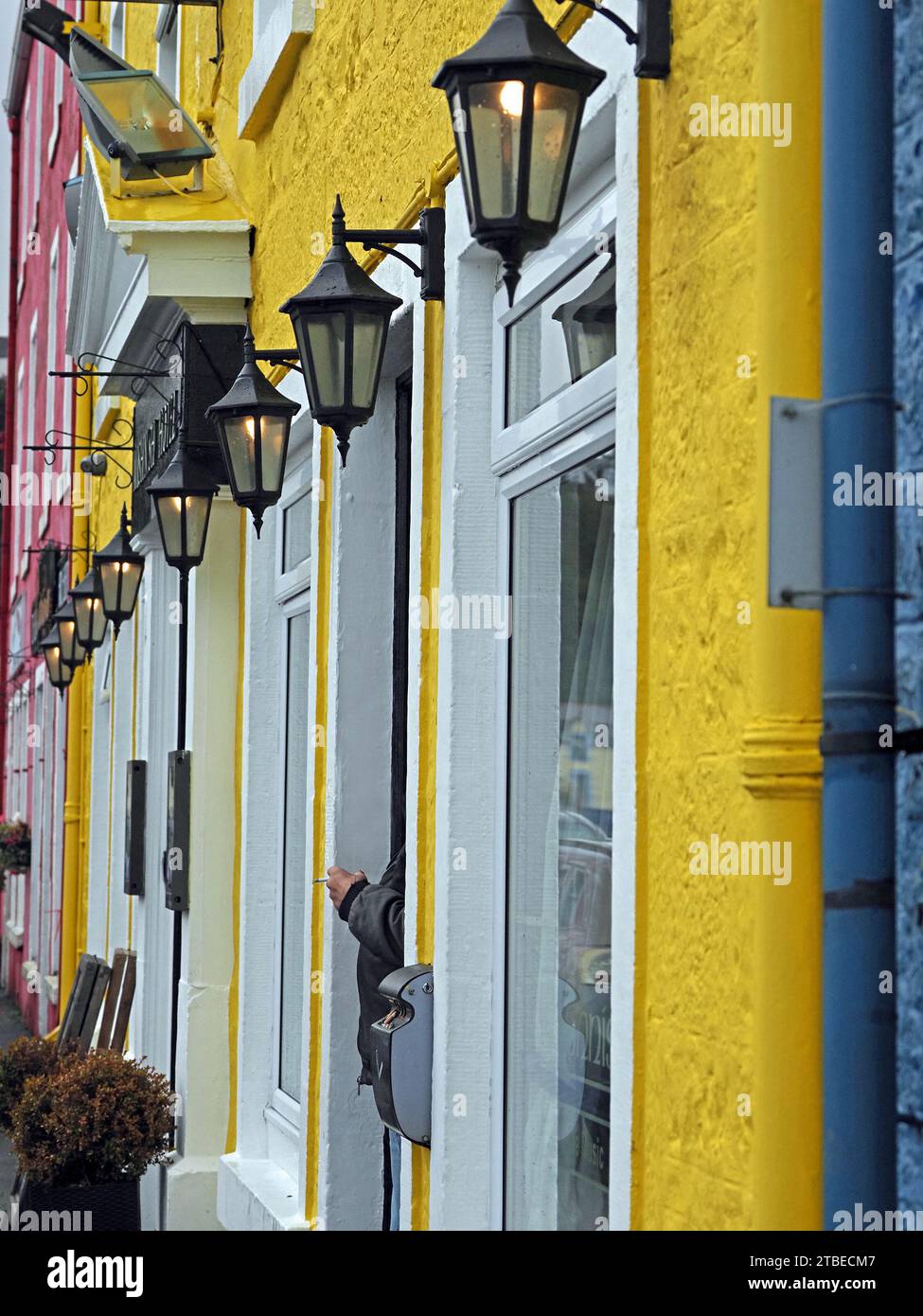 anonymous smoker's hand with cigarette among brightly painted facades of blue, yellow & red with white window frames beneath old-fashioned lanterns Stock Photo