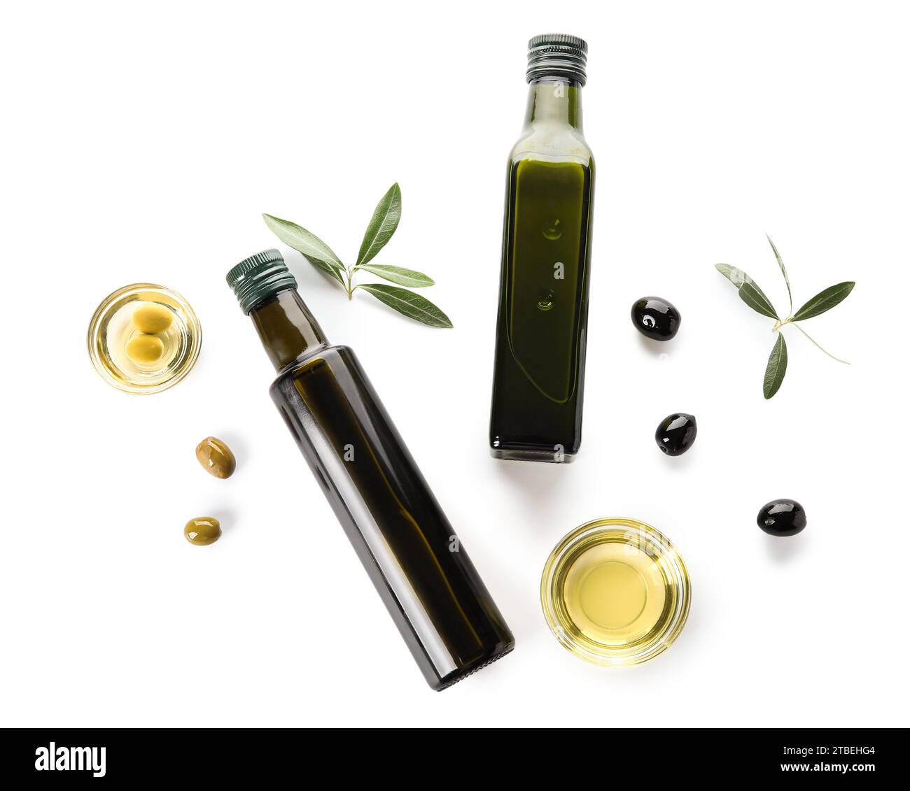 Glass bottles with olive oil, leaves and bowls on white background ...
