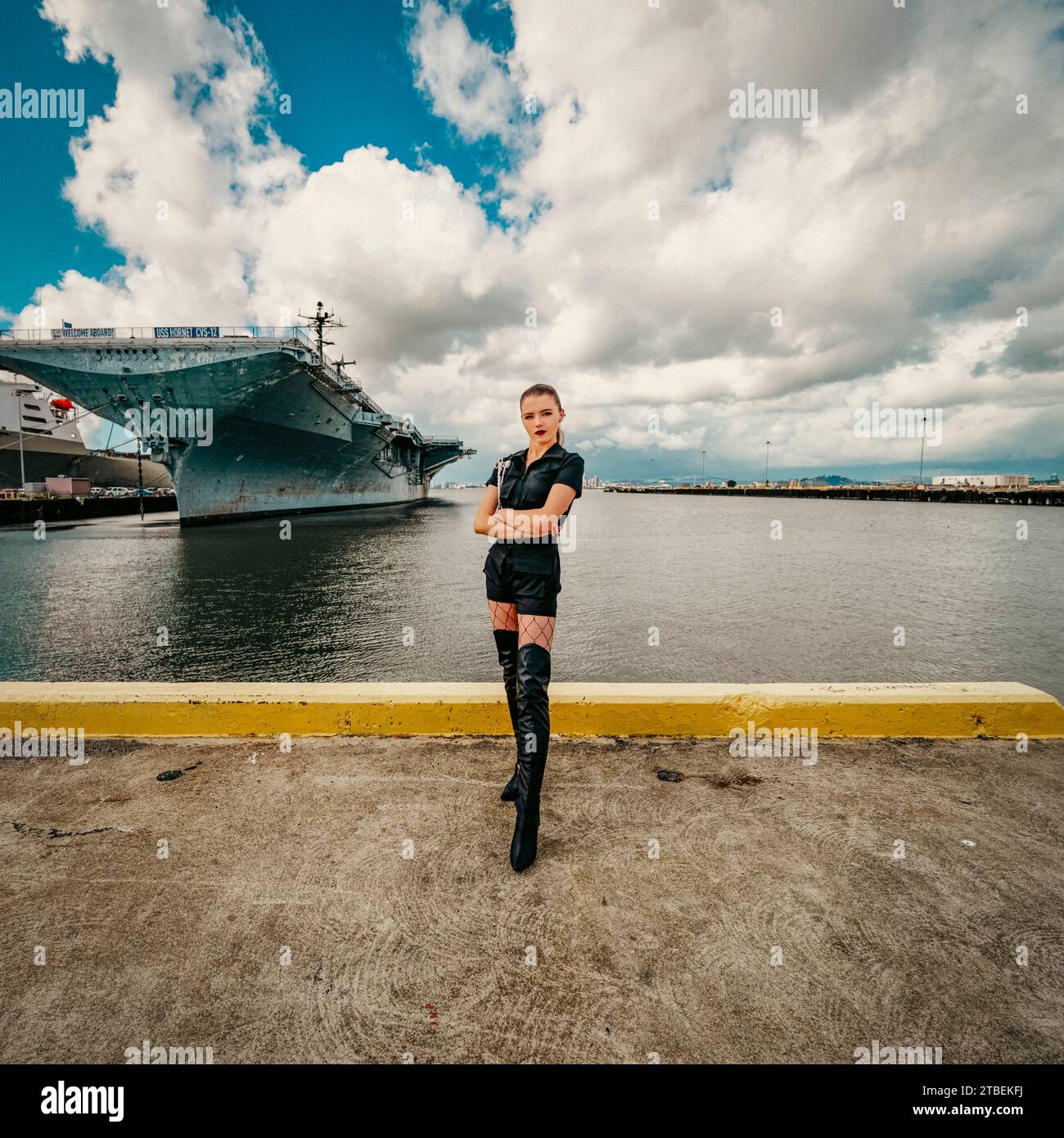 young goth woman standing in front of uss hornet aircraft carrier cloudy afternoon Stock Photo