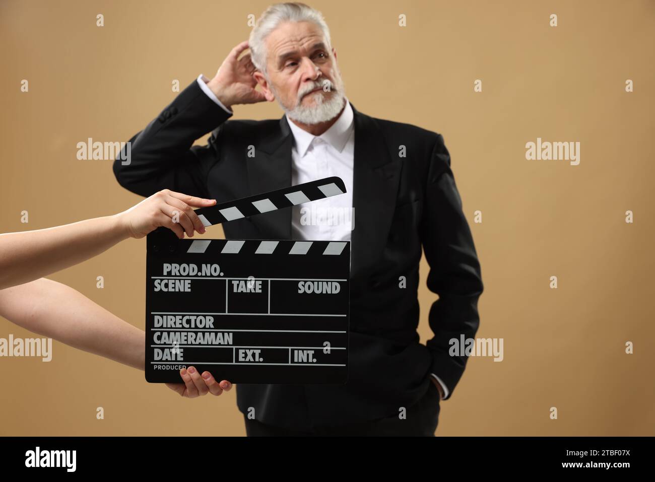 Senior actor performing role while second assistant camera holding clapperboard on beige background, selective focus. Film industry Stock Photo