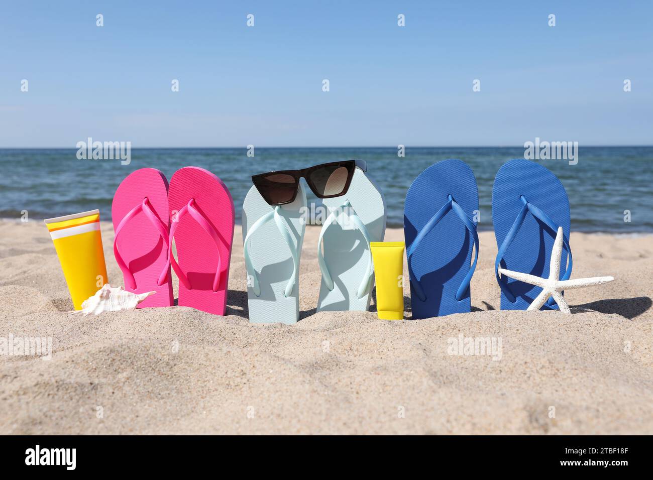 Stylish colorful flip flops with sunglasses and sunscreens on beach ...