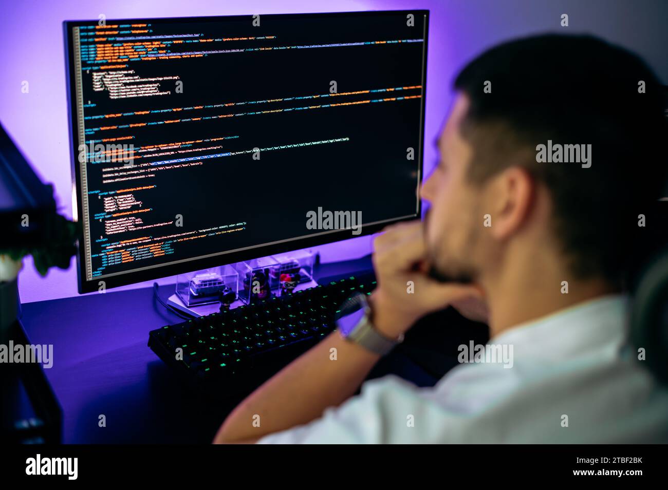 Successful male programmer sits in front of computer screen with programming code abstract technology background of software developer and computer script, working on web resource development Stock Photo