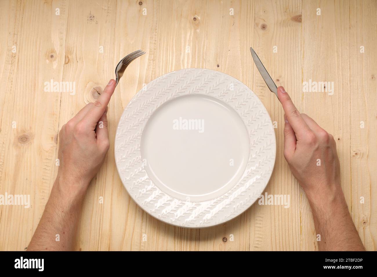 Man holding fork and knife near empty plate at wooden table, top view