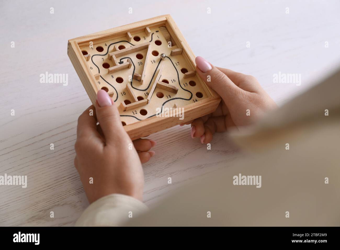 Woman holding wooden toy maze with metal ball at table, closeup Stock Photo