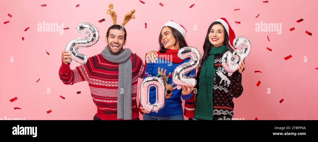 Group of happy male and female friends wearing sweaters celebrating Christmas 2023, studio shot portrait in pink color banner background Stock Photo