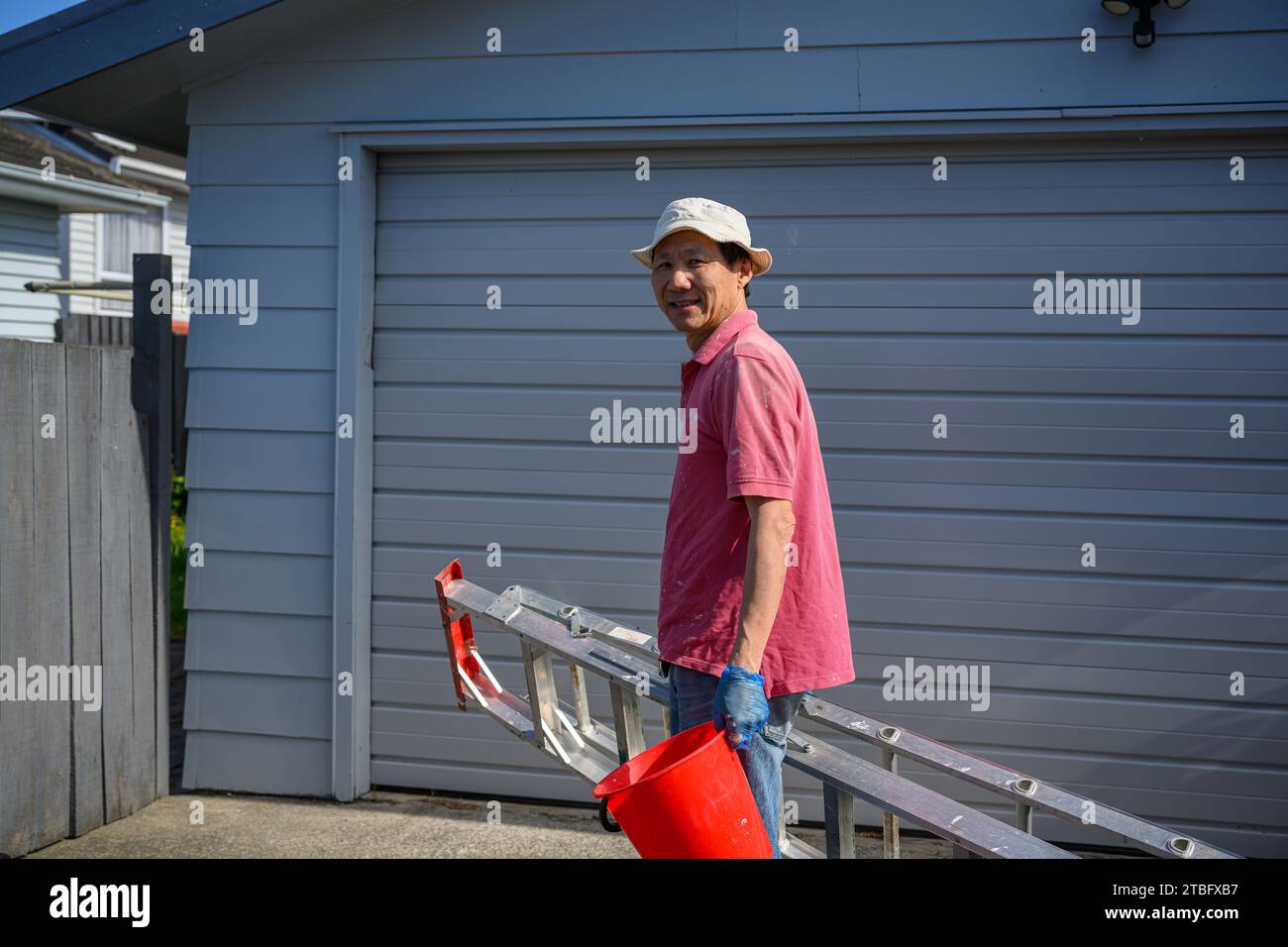 Man holding a ladder and red bucket after finishing work. Home