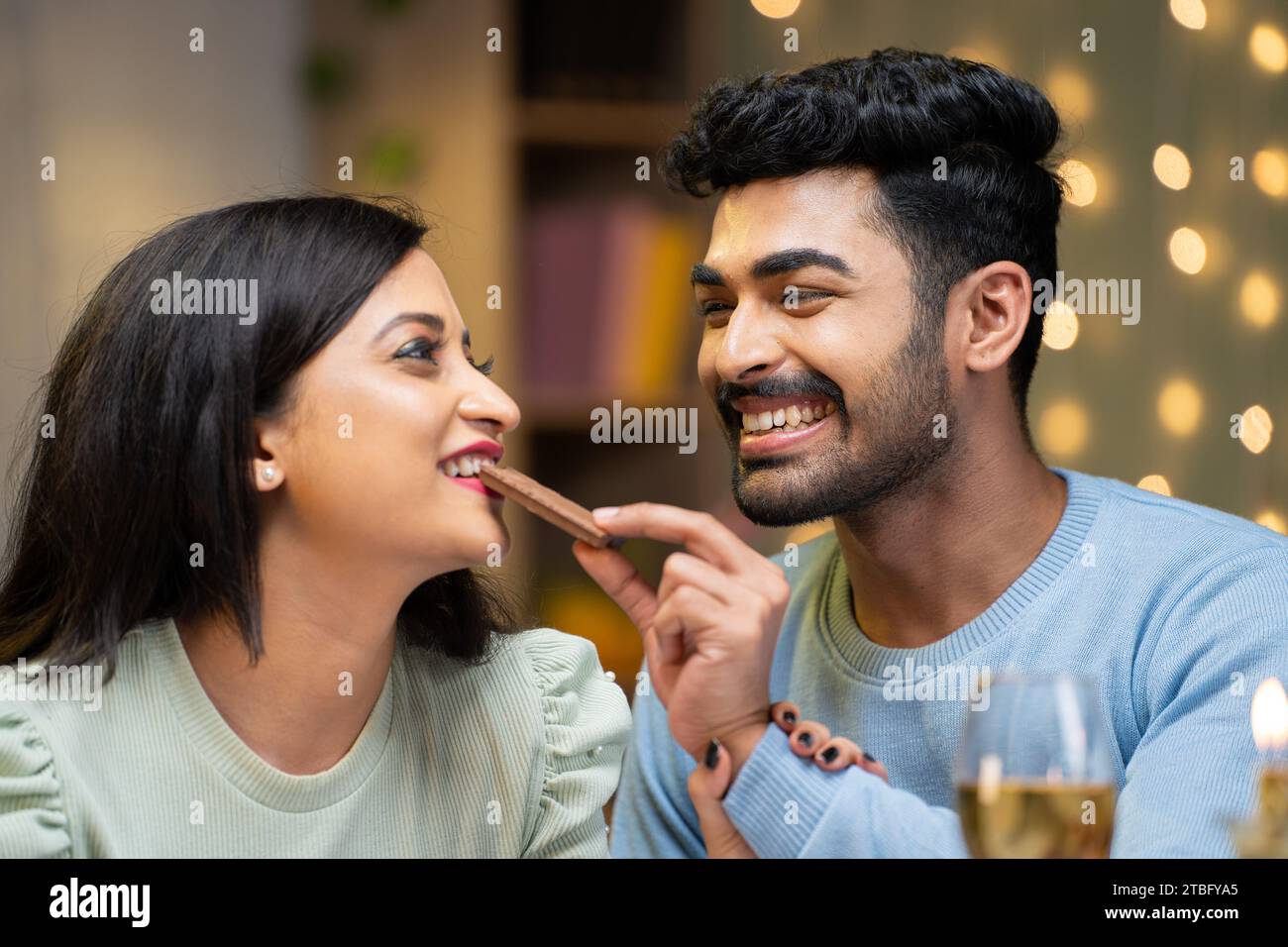 Happy young man giving chocolate byte to girlfriend during candle light