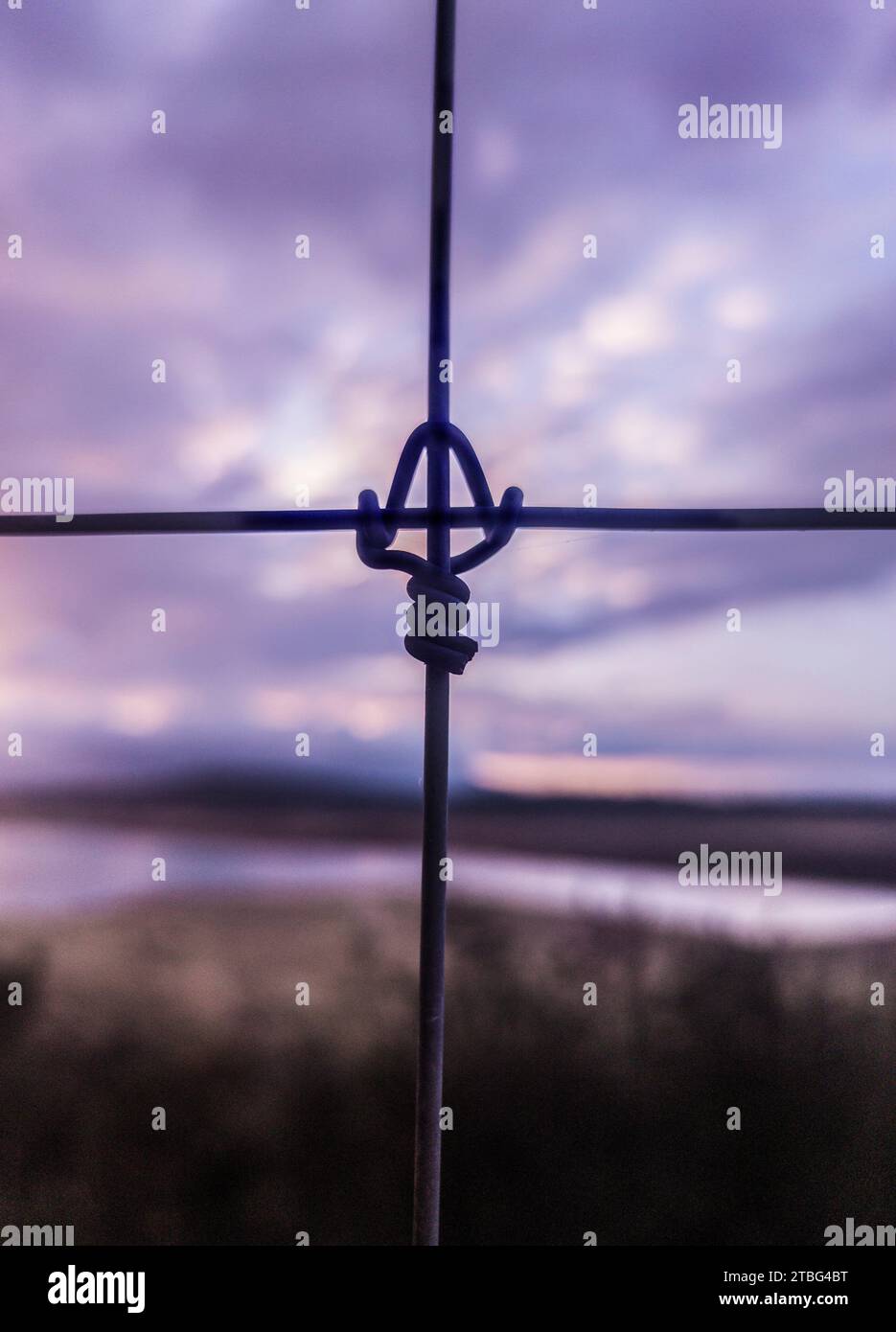 Metal fence cross lock knot at dawn. Reservoir at bottom Stock Photo