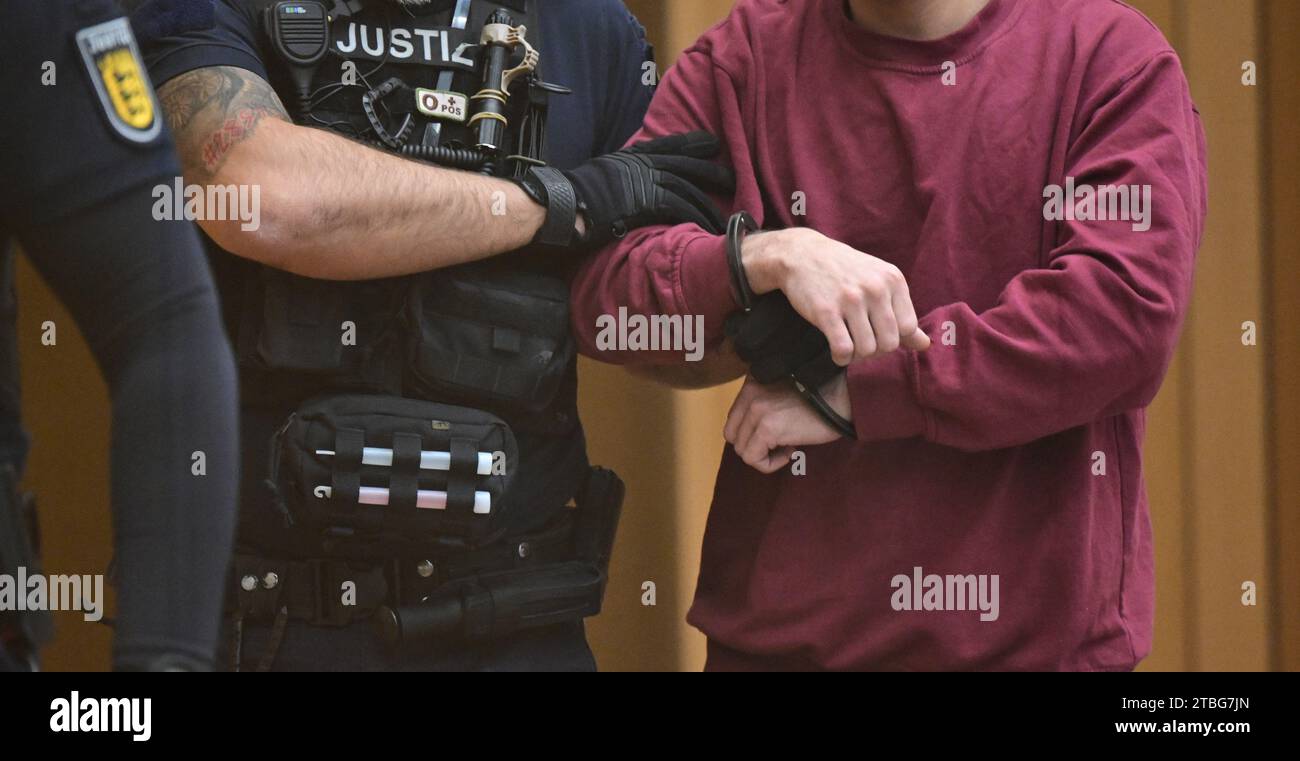 Stuttgart, Germany. 07th Dec, 2023. The defendant (r) is led into the courtroom at the start of a trial for fifteen counts of attempted murder. Two rival groups have been waging a bloody feud in the Stuttgart area for many months, culminating in a hand grenade attack on a mourning congregation in Altbach near Esslingen. The Stuttgart public prosecutor's office has filed charges including attempted murder against the 23-year-old suspected grenade thrower. Credit: Bernd Weißbrod/dpa/Alamy Live News Stock Photo