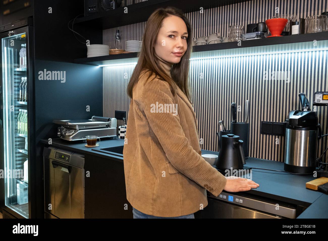 Calm young Caucasian cafe worker leaning on the counter in front of an