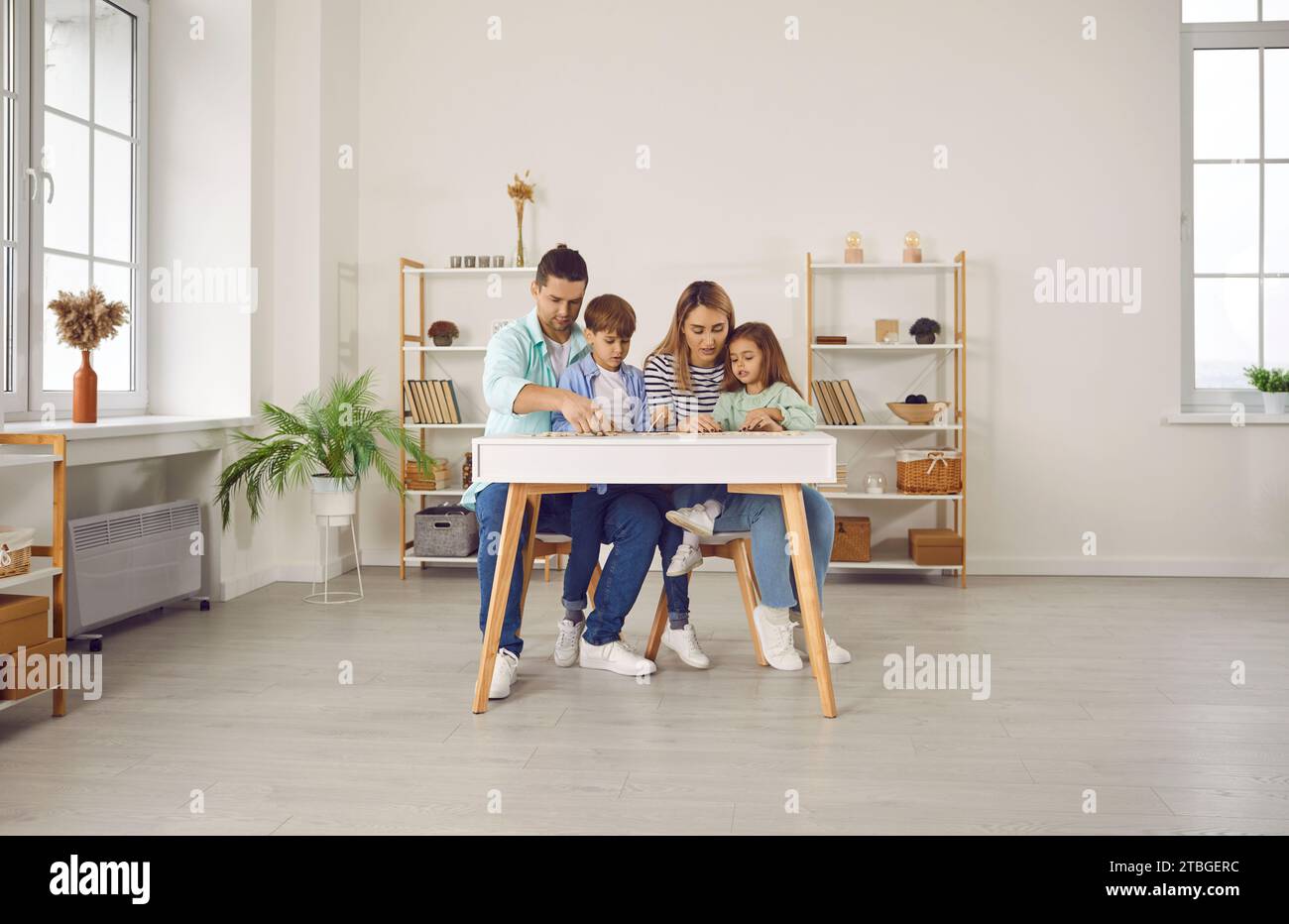 Parents playing with two kids in a puzzle in the living room at home. Stock Photo