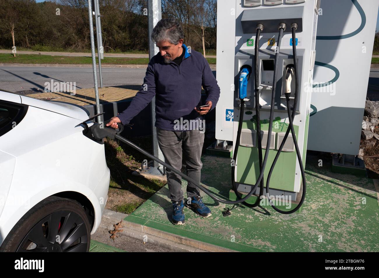 Man pluggin in a CCS plug to his Tesla Model 3 electric car at a public fast charging station Stock Photo