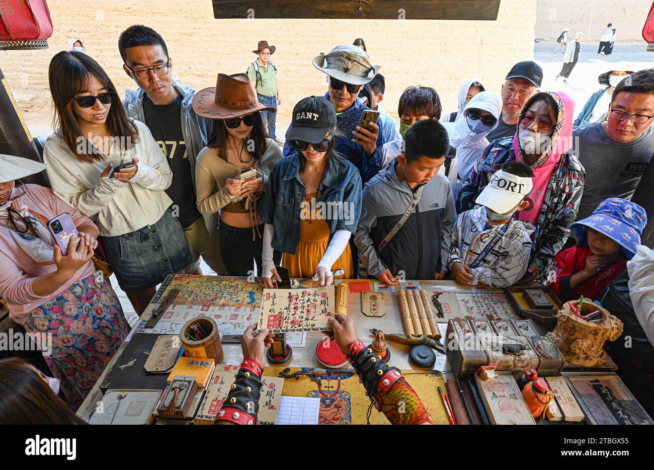 (231207) -- JIAYUGUAN, Dec. 7, 2023 (Xinhua) -- Visitors buy ancient 'visas' at Li Sen's stall at the Jiayu Pass scenic area in Jiayuguan City, northwest China's Gansu Province, July 14, 2023. Li Sen, 43, earns a living by playing the role of an ancient 'general' at the Jiayu Pass scenic area in the city of Jiayuguan, northwest China's Gansu Province. Visitors can buy ancient 'visas' at his stall. These documents are designed by Li and form an essential part of the role-play, allowing tourists to travel back into ancient China. Looking to the future, Li plans to systematically organize the Stock Photo