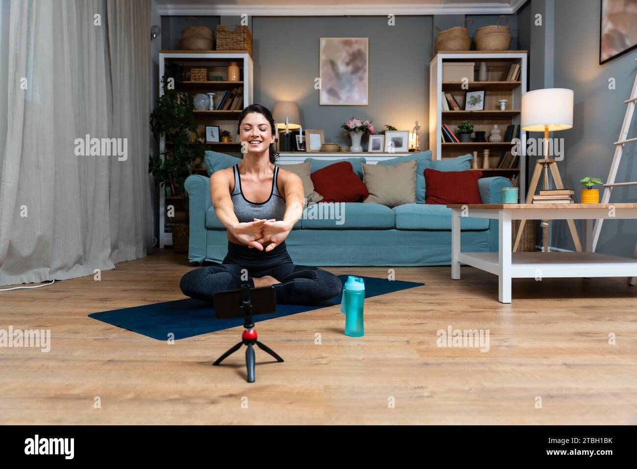 Attractive young woman learning new exercises watching online workout tutorials over her phone at home. Handsome female practicing yoga class having v Stock Photo