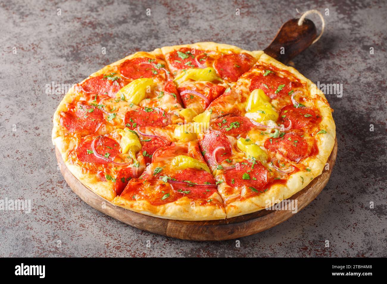 Sliced Pizza with salami, Pepperoncini , mozzarella, herbs and red onions close-up on a wooden board on the table. Horizontal Stock Photo