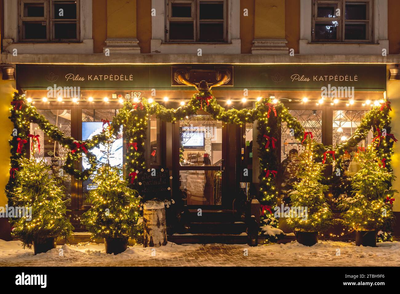 Beautiful entrance and windows of a restaurant with cozy Christmas decorations, wreath, garlands and lights in Vilnius old town, capital of Lithuania Stock Photo
