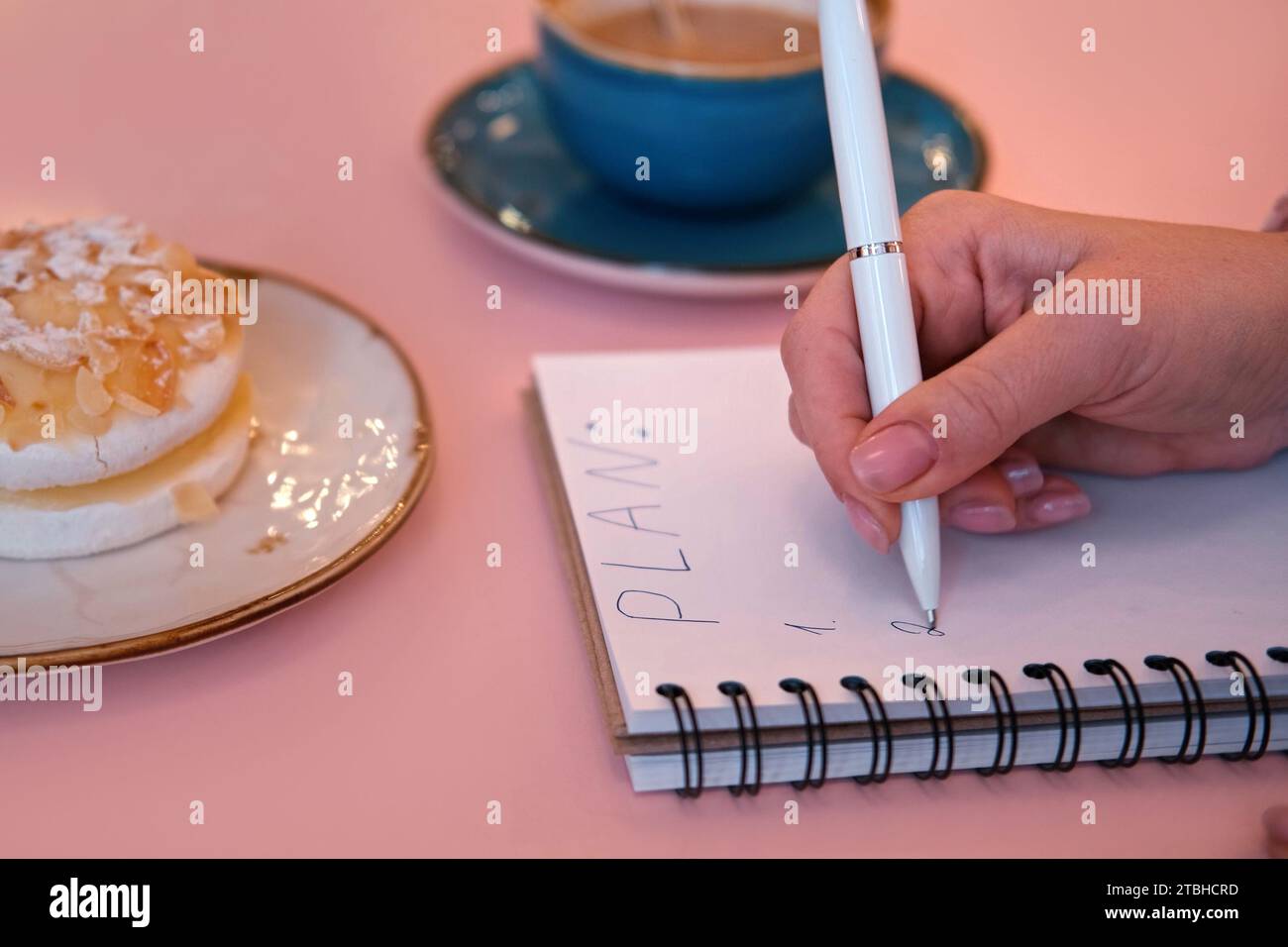 Woman Writing Plan in a Notepad Sitting on a Pink Cafe Table with ...