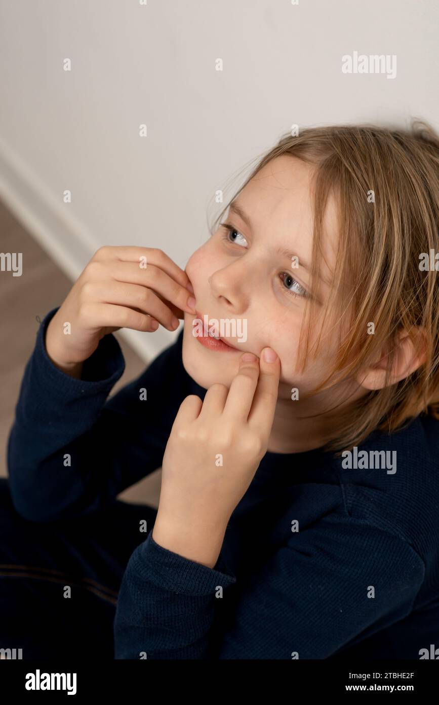 Lost in thought, a boy with flowing locks sits on the floor, encapsulating the innocence and contemplative spirit of childhood. Stock Photo