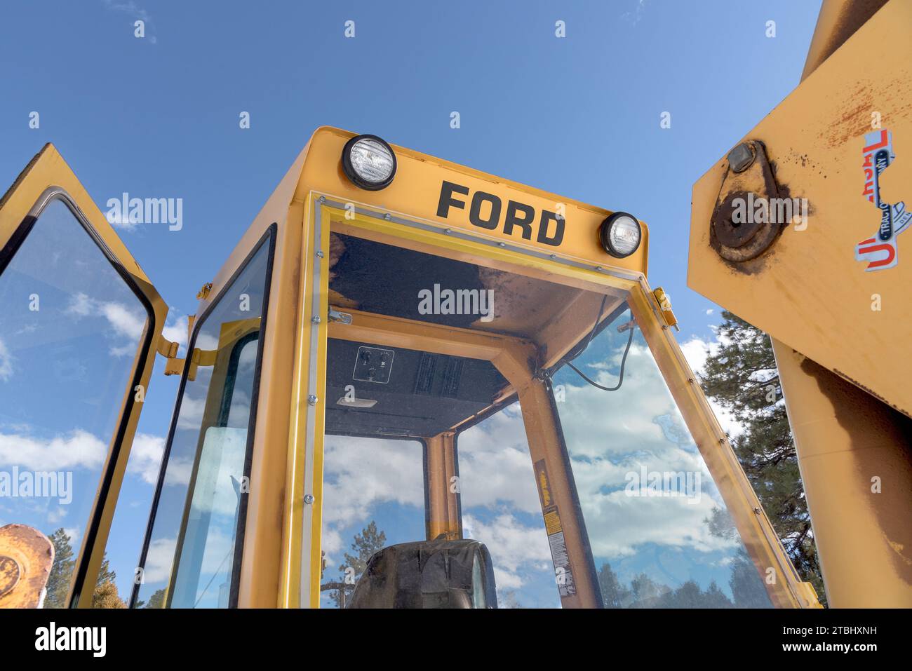 Looking up at the cab of a yellow Ford backhoe, blue sky with clouds in the background. Stock Photo