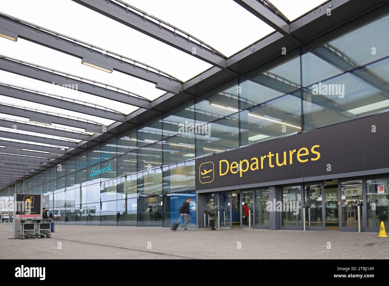 Gatwick Airport, UK, North Terminal, Departures entrance, exterior view. Passengers enter with luggage (blurred by motion). Stock Photo