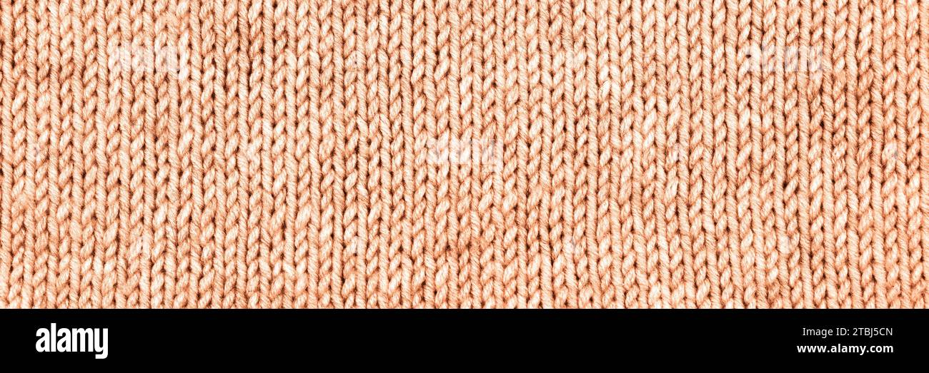 Demonstrating the colors of 2024 - Peach Fuzz. Knitted peach background. Large knitted fabric with a pattern. Close-up of a knitted blanket. Stock Photo