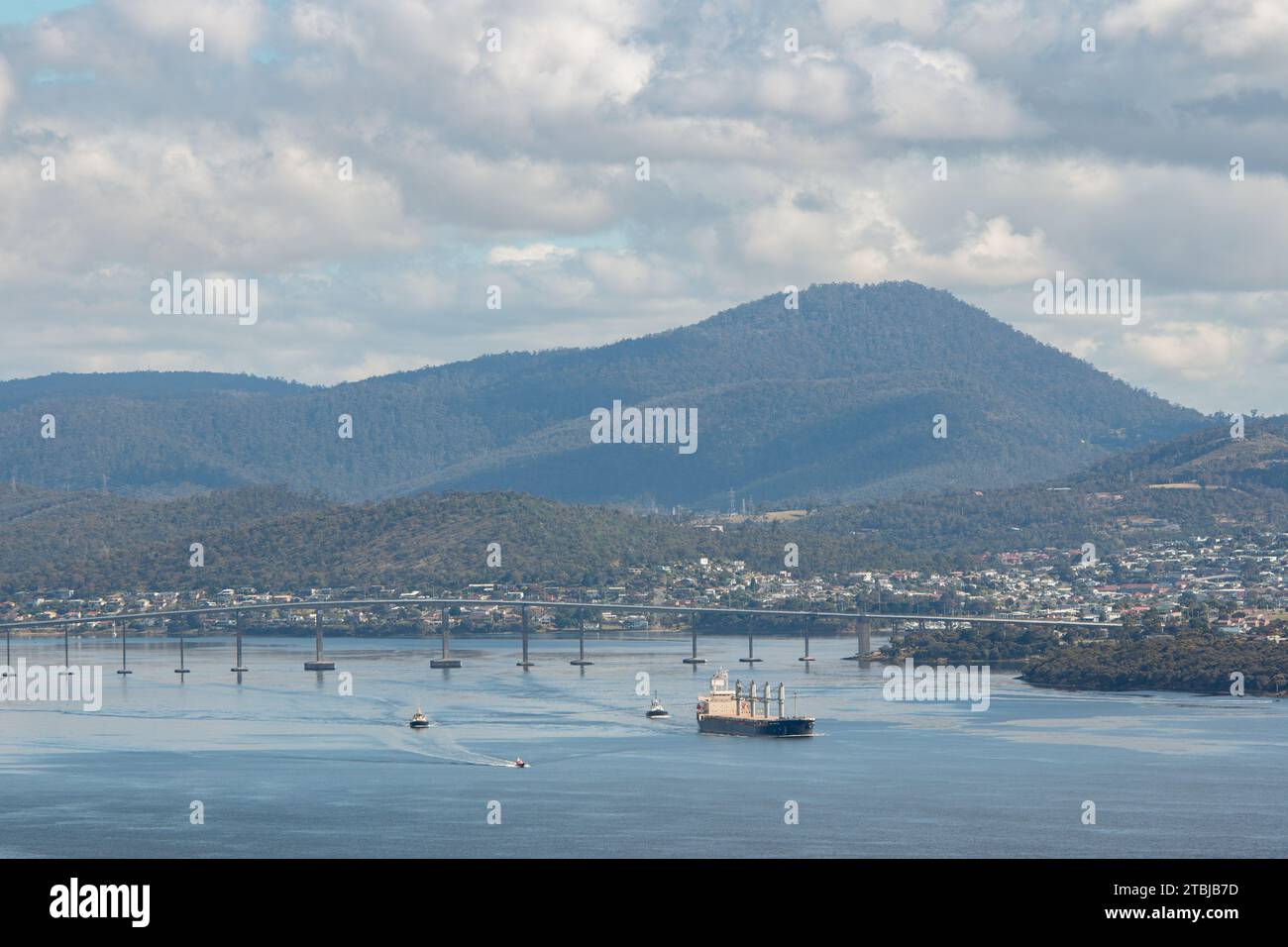 Hobart, Tasmania, Australia - December 12 2022: Derwent Estuary with cargo vessel and tug boarts cruising past Derwent bridge towards entrance of harb Stock Photo