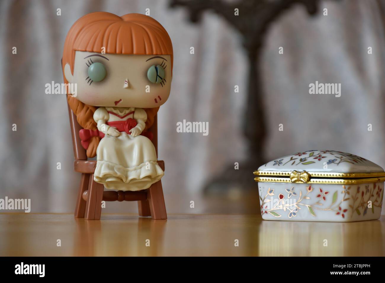 Funko Pop action figure of haunted doll Annabelle from The Conjuring horror films. Vintage interior, old candlestick, white printed jewelry box. Stock Photo