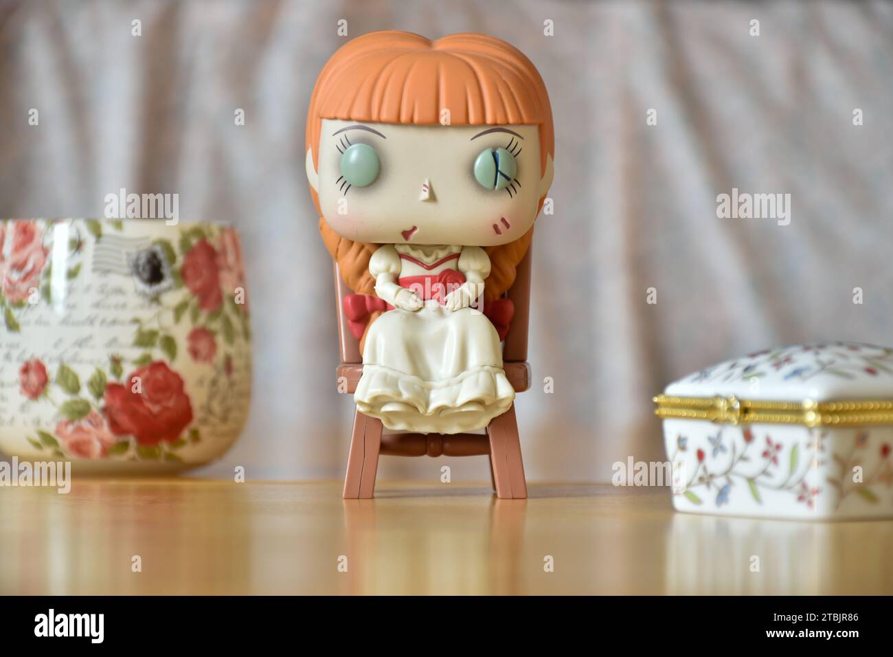 Funko Pop action figure of  haunted doll Annabelle from The Conjuring horror films. Vintage interior, white flower printed jewelry box and vase. Stock Photo