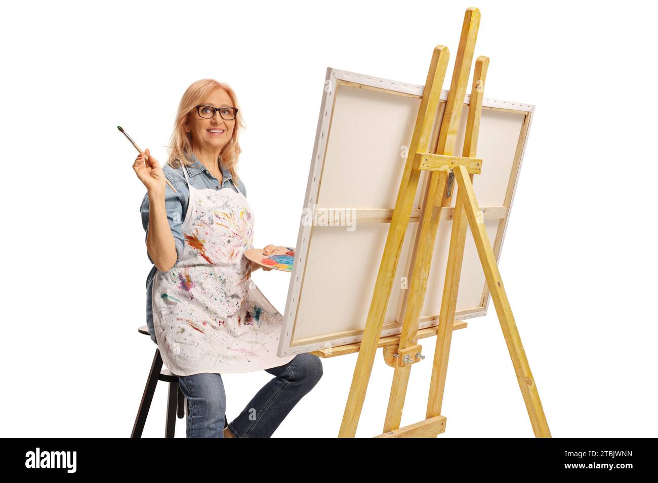 Middle aged woman sitting on a chair and painting on a canvas, hobbies and leisure concept Stock Photo