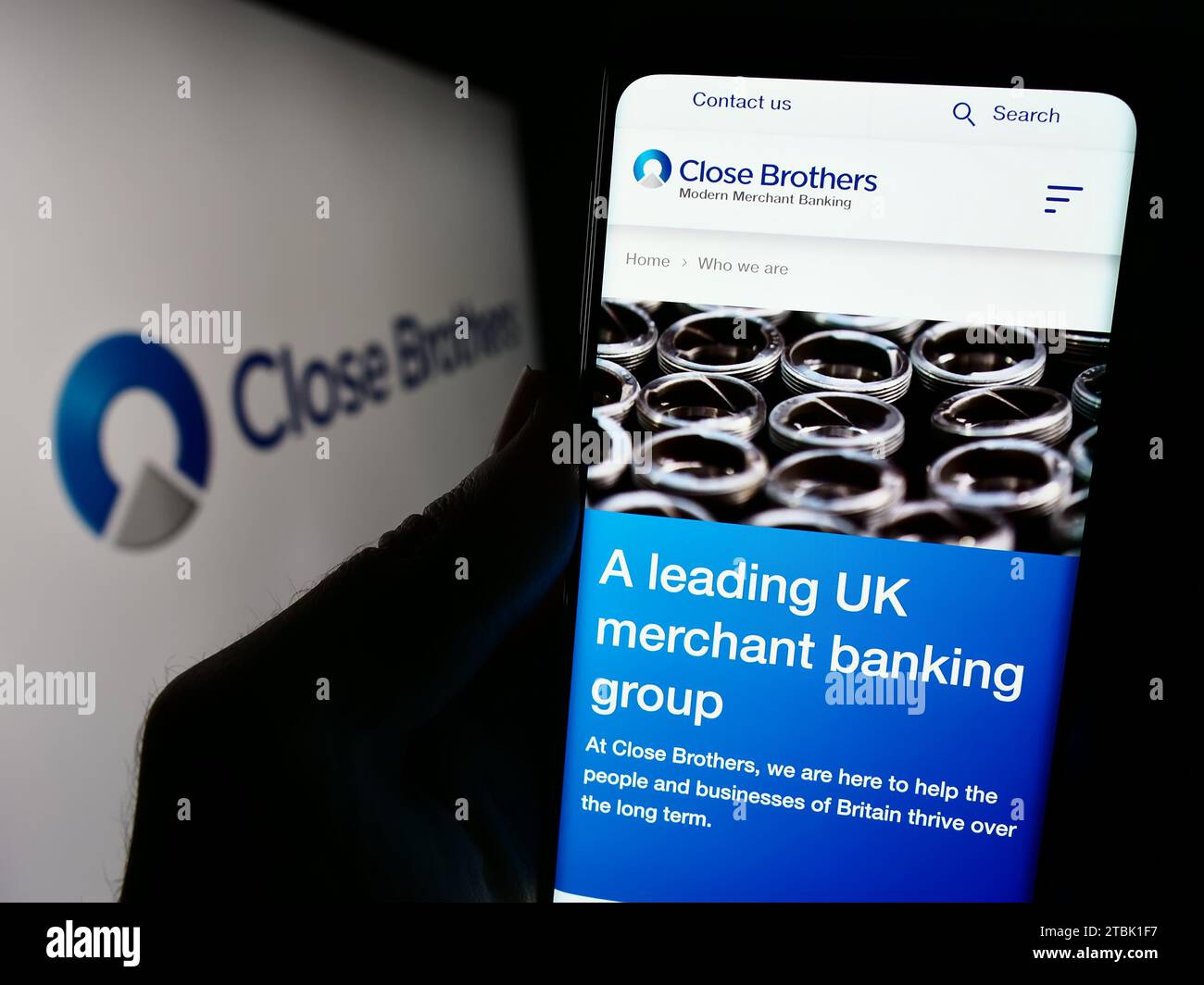 Person holding mobile phone with web page of British merchant bank company Close Brothers Group plc with logo. Focus on center of phone display. Stock Photo