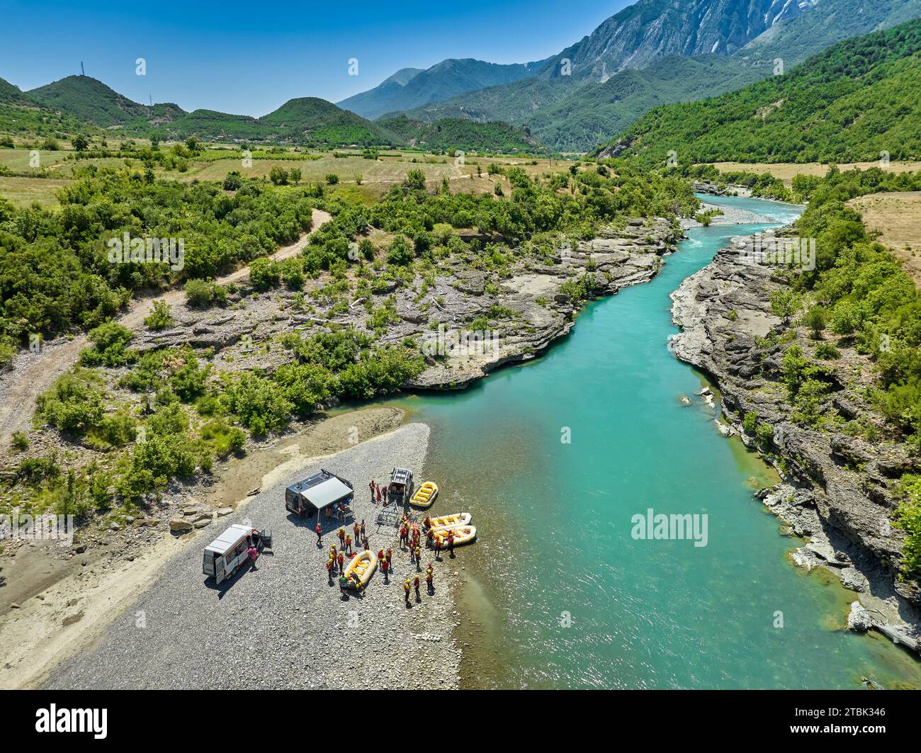 White water rafting.  Vertical drone view  of a group cars, yellow rafts and people ready to float on blue-green river Vjosa, Albania. Stock Photo