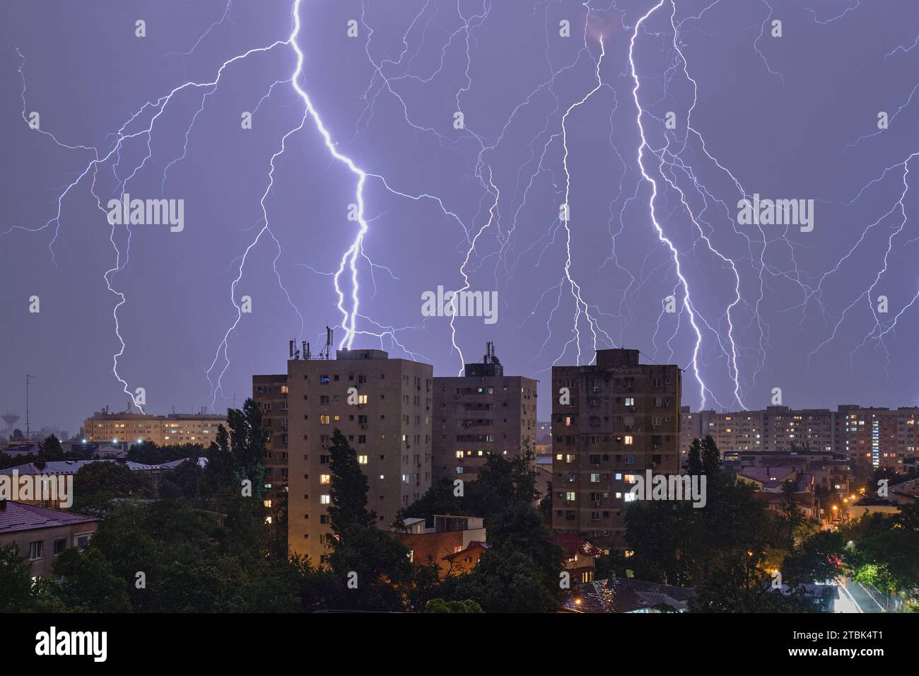 Multiple lightning strikes and thunderstorm over city buildings, at night. Weather phenomena. Stock Photo