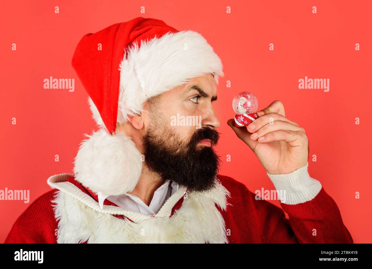 Christmas decoration. Bearded man in Santa hat with small snowglobe. Christmas snowball with little with Santa Claus inside and floating bright snow Stock Photo