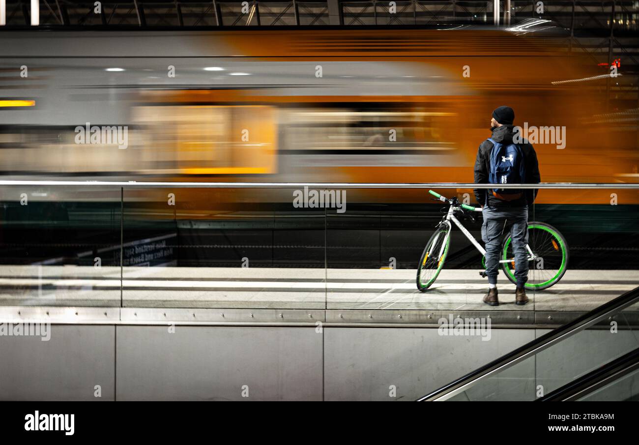 A man in a blue shirt and black pants stands in an underground subway station, waiting for the train to arrive Stock Photo