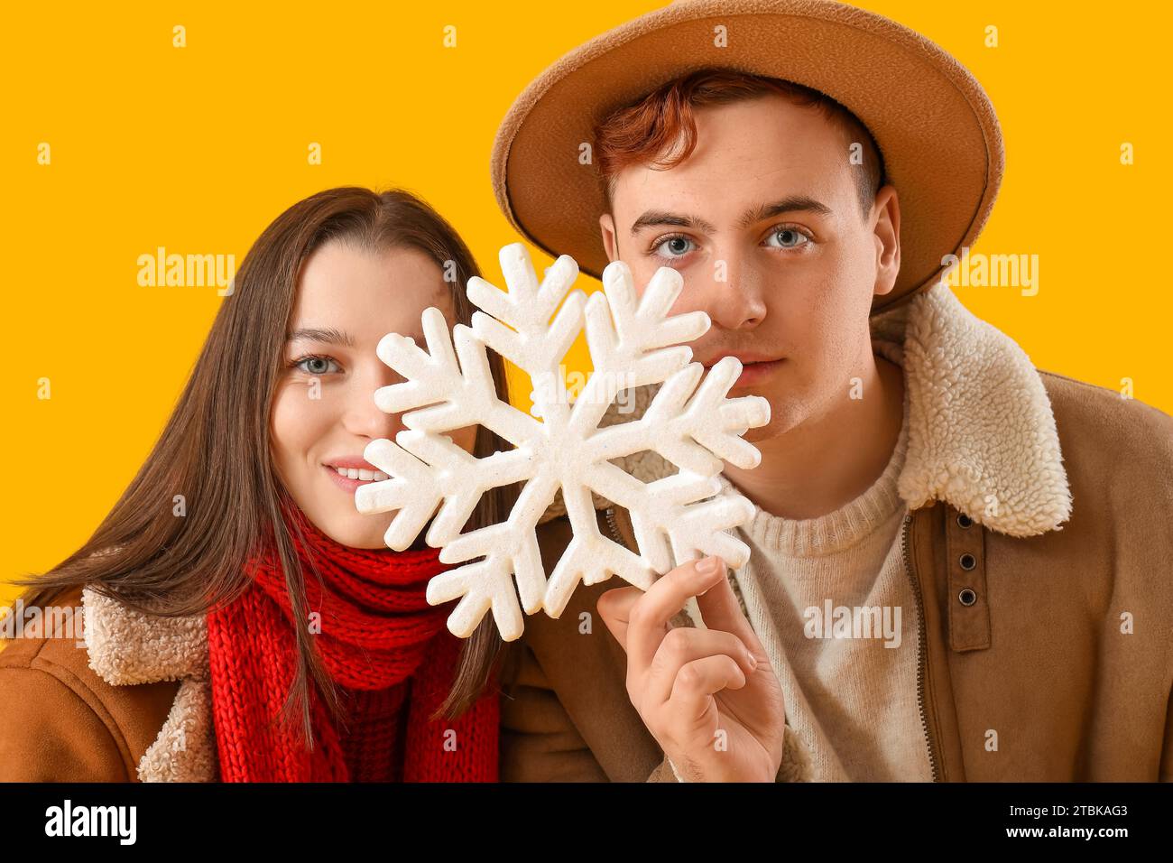 Young couple in winter clothes with snowflake on yellow background, closeup Stock Photo