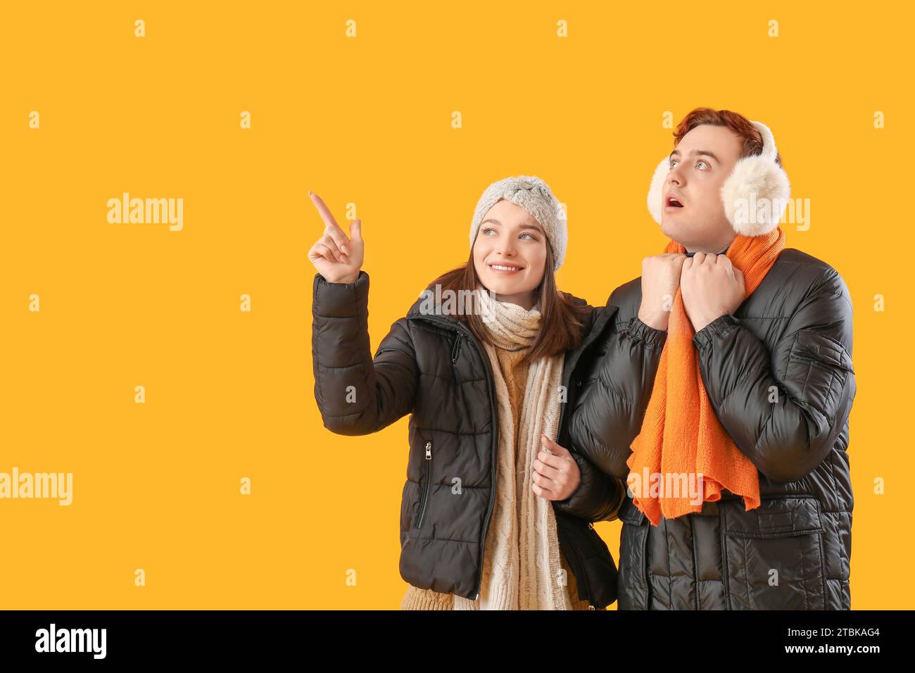 Young couple in winter clothes pointing at something on yellow background Stock Photo