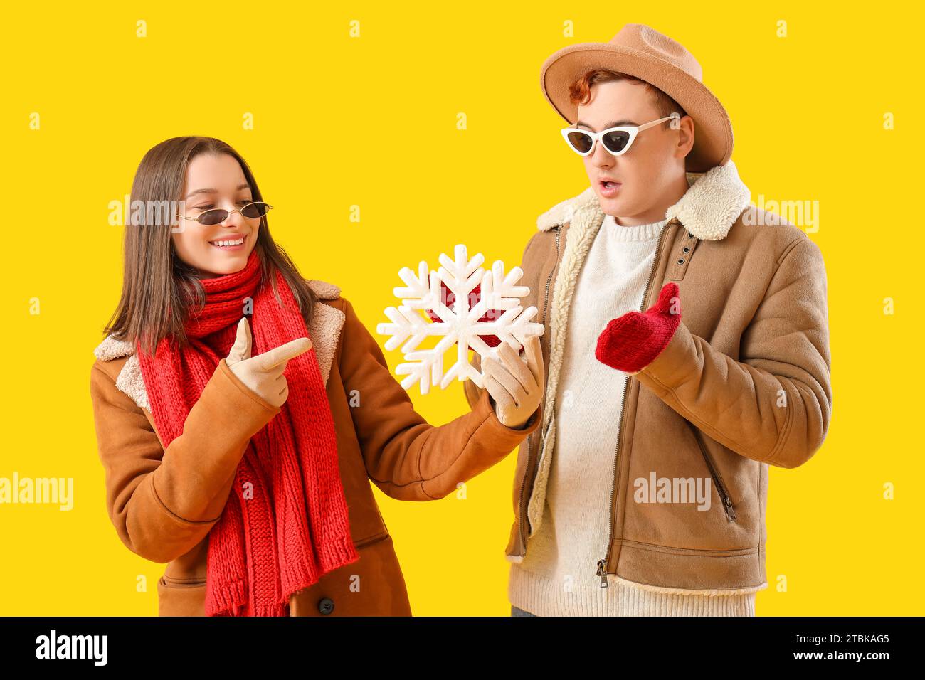 Young couple in winter clothes with snowflake on yellow background Stock Photo