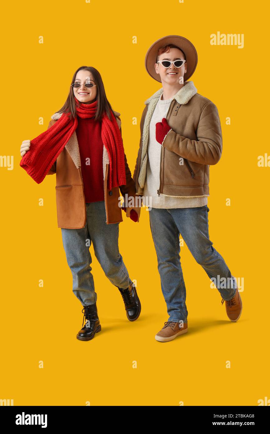 Young couple in winter clothes walking on yellow background Stock Photo